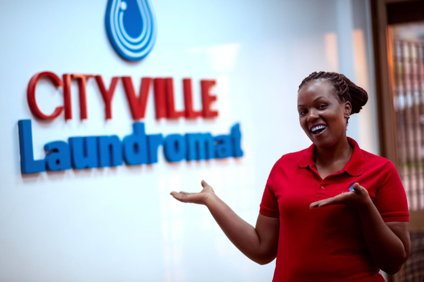 Our Branch Manager welcoming evryone to CityVille Laundromat pointing at the CityVille Laundromat logo on the wall